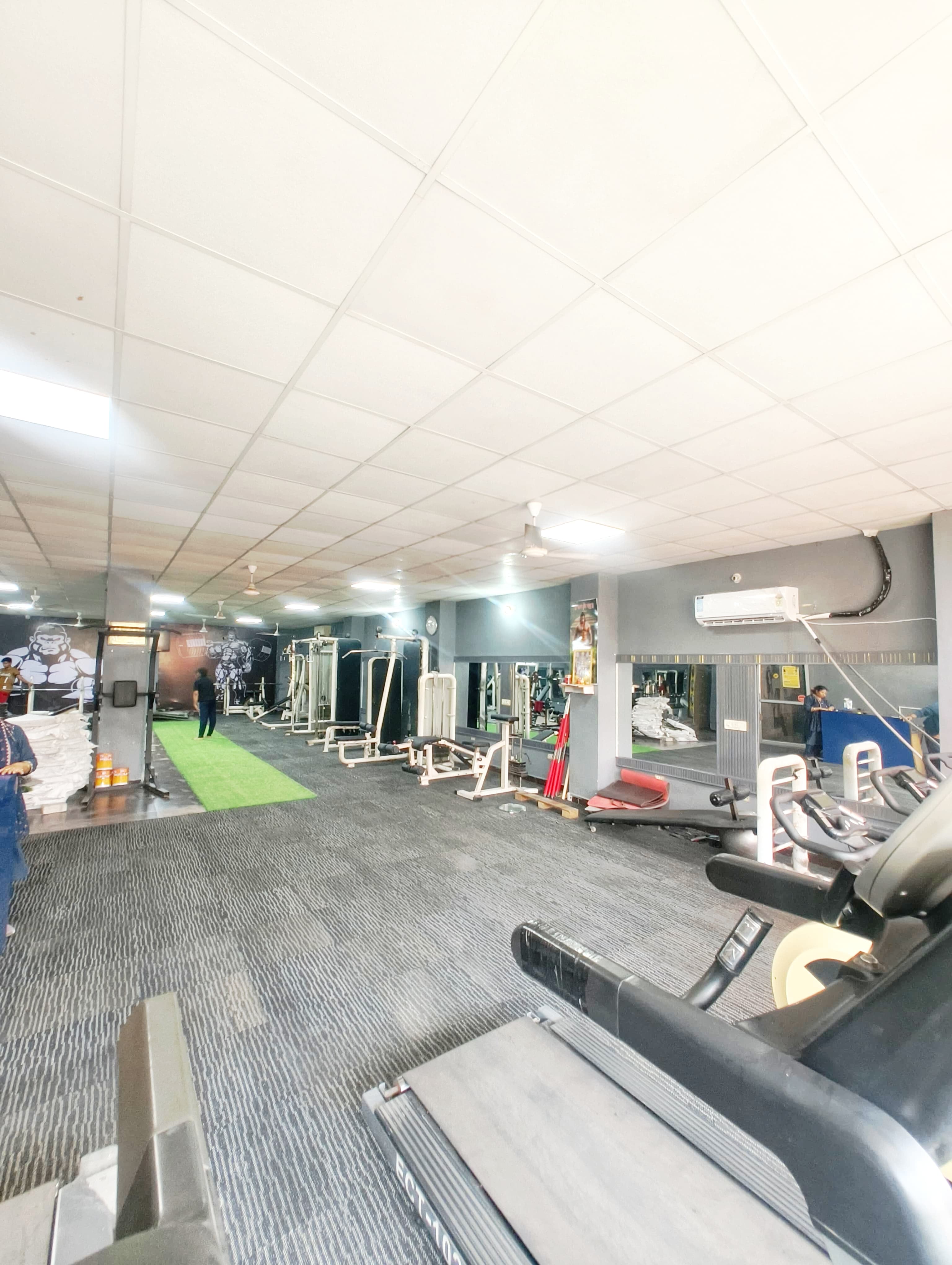 Spacious gym interior featuring treadmills, weightlifting equipment, and a green artificial turf workout lane.