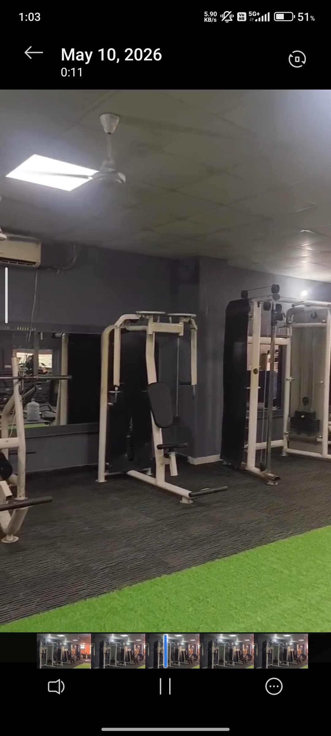 Gym interior featuring weightlifting machines, grey walls, and a section of green artificial turf.